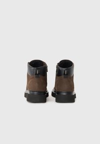 Botine din suede maron cu o guler din piele neagră, dotate cu un fermoar lateral și o talpă din cauciuc texturat. Design simplu și funcțional.