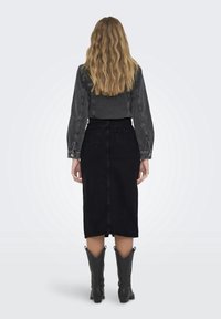 Svart midikjol i denim med hög midja, kombinerad med en mörkgrå denimtop. Bärs med svarta cowboyboots; synliga sömmar.