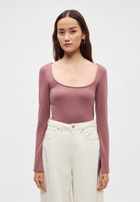 Pika varrukaga lavendlivärvi bodiis ümarate kaelustega, valmistatud pehmest kangast, mis on kombineeritud kõrge vöökohaga valgete laia säärega pükstega, millel on taskud.