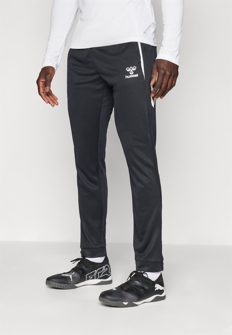 Musta spordipüksid valge küljeribaga ja logoga, valmistatud siledast kangast. Kombineeritud mustade spordijalatsitega, millel on valged aktsendid.