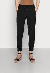 Pantalones jogger negros, ligeros, con puños elásticos, cintura ajustable con cordón y bolsillos laterales. Combinando con sandalias espadrille negras.