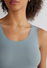 Světle modrý top bez rukávů s kulatým výstřihem; hladká textura a přiléhavý střih. Akcent na rameni a minimální viditelné švy.