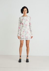 Hvit blomsterkjole med rosa og blå mønstre, lange ermer med breddeender, og tettsittende design. Bært med svarte sko med nagler.