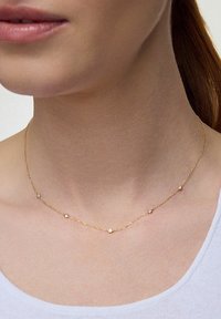 Złoty naszyjnik z łańcuszka z małymi, okrągłymi, metalowymi koralikami równomiernie rozmieszczonymi wzdłuż długości. Prosty design z delikatną teksturą.