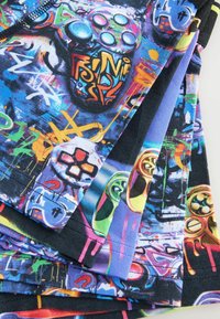 Bunte Grafikstoff mit verschiedenen Spielcontrollern und abstrakten Mustern in Blau, Schwarz, Neon-Grün, Gelb und Orange.