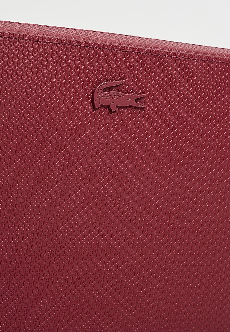 Sac texturé rouge avec un accent de logo en relief. Le matériau semble durable avec un motif géométrique, mettant en valeur un design élégant.