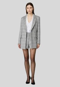 Blazer doppiopetto in plaid grigio abbinato a pantaloncini su misura coordinati. Caratterizzato da un design strutturato, rever netti e tessuto dalla texture liscia.