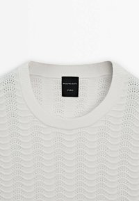 Pull tricoté blanc avec motif ondulé et petits détails ajourés, col rond et étiquette noire Massimo Dutti Studio à l'intérieur du col.