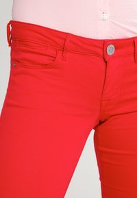 Røde cowboybukser i denim har et tætsiddende design, fem lommer og en sølvfarvet knaplukning med en glat tekstur og minimal syning.