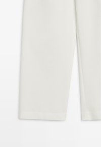 Lower section of off-white tailored pants with straight legs and clean hem against a plain background.