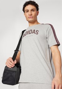 Pelēks īsām piedurknēm T-krekls ar "ADIDAS" logotipu bordo krāsā, ar bordo svītrām uz pleciem. Melna soma ar sieta akcentiem.