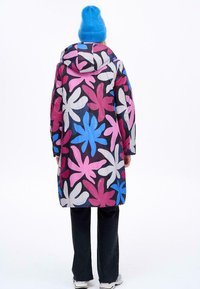 Barevný dlouhý kabát s květinovým vzorem v růžové, modré a bílé na černém pozadí; má kapuci a široké rukávy.