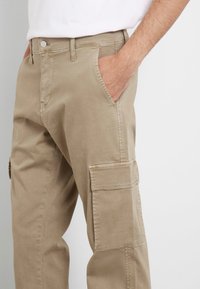 Beige cargo broek gemaakt van een katoenmix, voorzien van zijzakken, een relaxte pasvorm en zichtbare stiksels.