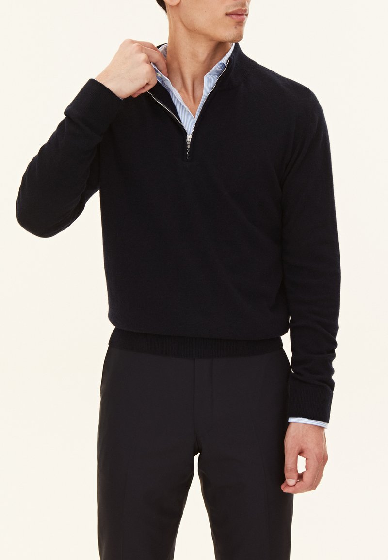 Pull-over en maille bleu marine avec un col zippé d'un quart, des poignets et un ourlet côtelés, porté sur une chemise rayée bleu clair.