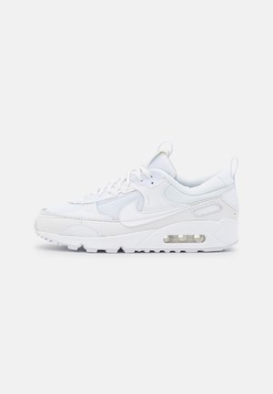 Baskets de sport blanches avec panneaux en mesh et en cuir, coussin d'air visible dans la semelle, semelle épaisse, fermeture à lacets et logo Swoosh de Nike sur le côté.
