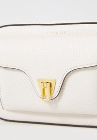 White textured leather handbag with a gold triangular clasp and contrasting border trim. Features embossed logo on the front.
