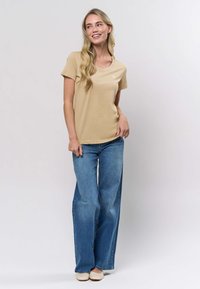 Béžové bavlněné tričko s krátkými rukávy, kulatým výstřihem a volným střihem, doplněné světle modrými širokými džínami a béžovými tkanými nazouvacími botami.