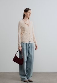 Απαλό ροζ ζακέτα με κουμπιά, σε συνδυασμό με ανοιχτό μπλε τζιν με φαρδιά μπατζάκια. Καφέ τσάντα και μπεζ παπούτσια. Λεία υφή και απλός σχεδιασμός.