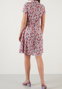 Květinové šaty s růžovým pozadím, krátkými rukávy, přiléhavým pasem a rozšířenou sukní. Nosené s levandulovými sandály na širokém podpatku.