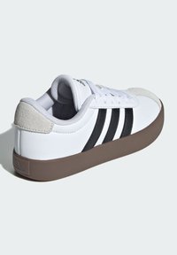 Biały sneaker z czarnymi paskami, gumową podeszwą i zamszowym czubkiem. Posiada wyściełany kołnierz i sznurowane zapięcie.