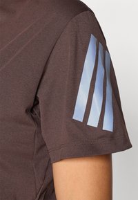 Brązowa koszula z krótkim rękawem o gładkiej fakturze, z graficznym wzorem trzech jasnoniebieskich pasków na lewym rękawie.