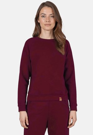 Burgundské crewneck svetr s uvolněným střihem, žebrovanými manžetami a pasem; na lemu se nachází malá kožená štítek s logem.