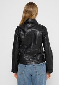 Veste en cuir noir au design ajusté, avec col cranté et poignets zippés. Présente des coutures au dos et une texture lisse et brillante.