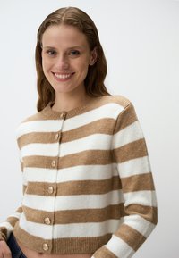 Bruine en witte gestreepte cardigan van zacht materiaal, met een ronde halslijn en zes knopen aan de voorkant, cropped lengte.