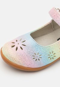 Zapato Mary Jane brillante con arcoíris, con cortes florales, una correa ajustable rosa y una suela de goma marrón. Acabado suave y texturizado.
