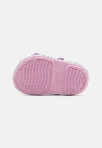 Jasnofioletowe obuwie z teksturową różową podeszwą, z wzorem w rowki i nadrukowanym logo. Zaprojektowane z myślą o komforcie i łatwości noszenia.