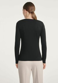 Czarna bluzka z długim rękawem o okrągłym dekolcie, gładkiej fakturze i dopasowanym kroju, w połączeniu z jasnymi spodniami.