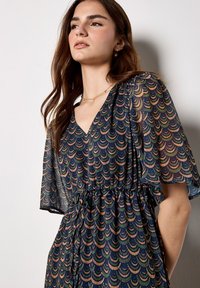 Sukienka w kwiatowy wzór w kolorze granatowym z falującym wzorem w zieleni, złocie i koralu. Posiada krótkie, rozkloszowane rękawy oraz tunele do sznureczka w pasie.