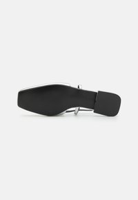 Silver high-heeled shoe with a pointed toe, sleek design, black textured sole, and a strap across the ankle, showcasing modern style.