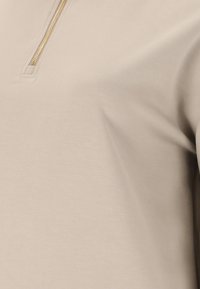 Beige tröja med halvdragkedja. Slät textur med subtil lyster. Har en gulddetalj vid dragkedjan för en modern känsla.