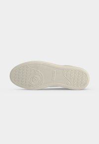 Semelle d'une chaussure beige avec motif antidérapant texturé, logo circulaire près du talon et taille 42 indiquée près de la zone de la voûte plantaire.