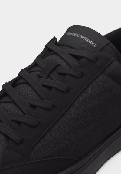Κοντινό πλάνο μαύρου sneaker Emporio Armani με υφασμάτινο μοτίβο λογότυπου, μαύρα κορδόνια και γλώσσα με λογότυπο σε λευκό φόντο.