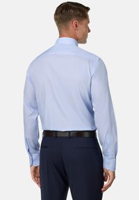 Jasnoniebieska koszula z długimi rękawami i guzikami przy mankietach, ozdobiona delikatnym wzorem w kratę, w połączeniu z ciemnymi spodniami i czarnym paskiem.