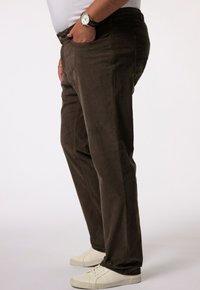 Bruine ribfluweel broek met een rechte pasvorm, voorzien van zijzakken en een gladde textuur. Gecombineerd met witte sneakers.