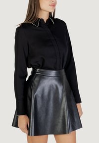 Maglietta nera a maniche lunghe con colletto decorato da perle, abbinata a una gonna nera in pelle a vita alta con forma svasata e texture liscia.