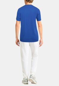 T-shirt di cotone blu con maniche corte e collo rotondo, abbinata a pantaloni bianchi e sneakers grigie, vista da dietro.