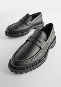 Sorte læder loafers med en struktureret finish, lav profil, mokkasin-syninger og tyk gummisål med en mønster for bedre greb.