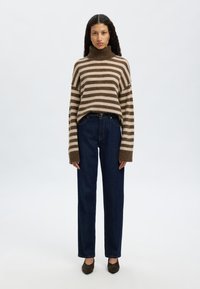 Randig polotröja i brunt och beige, kombinerad med mörkblå högmidjade jeans. Mjuk textur med lös passform och långa ärmar.