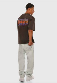 Svart t-skjorte med korte ermer med flerfarget tekst på baksiden; kombinert med lyse, løse jeans og hvite joggesko.