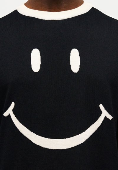 Μαύρο πουλόβερ με μεγάλο λευκό σχέδιο ευτυχισμένου προσώπου που διαθέτει δύο οβάλ μάτια και καμπύλο χαμογελαστό στόμα στο στήθος.