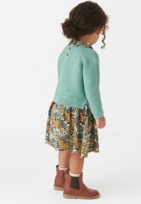 Tyrkysový pletený svetr s květinovou sukní v oranžových, modrých a hnědých tónech; hnědé kotníkové boty s vlnitými okraji.