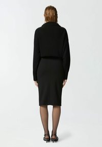 Crni rebrasti pulover s skraćenim dizajnom, u kombinaciji s uskom crnom suknjom. Prozirne crne čarape i crne štikle upotpunjuju izgled.