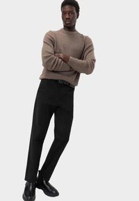 Brun ribbet sweater, sorte bukser og sorte støvler. Sweateren har en klassisk rund hals og en afslappet pasform, mens bukserne har en tætsiddende design.