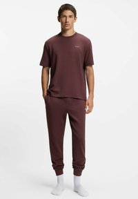 Burgunderrotes, strukturiertes Baumwoll-T-Shirt mit kurzen Ärmeln und kleinem Logo, kombiniert mit passenden, zulaufenden Sweatpants und weißen Socken.