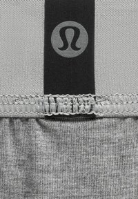 Tessuto grigio con una texture liscia presenta una fascia nera nella parte superiore con un logo circolare e un orlo cucito.