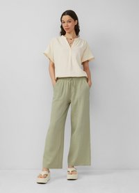 Crème top met korte mouwen en v-hals, gecombineerd met lichtgroene wijde broek met een elastische tailleband, en platform sandalen.